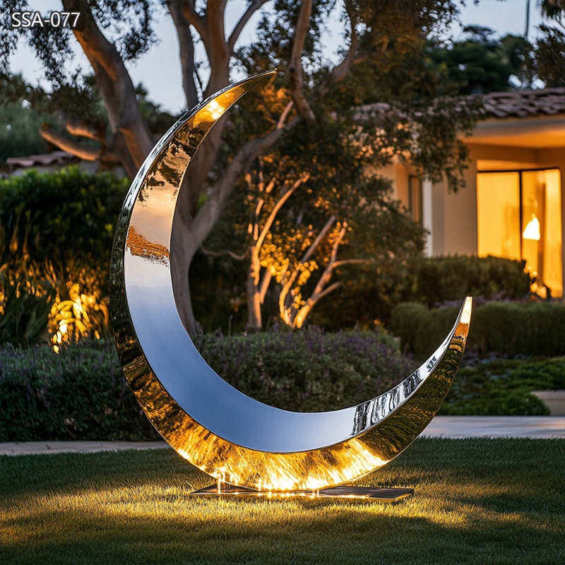 large stainless steel crescent moon sculpture at night